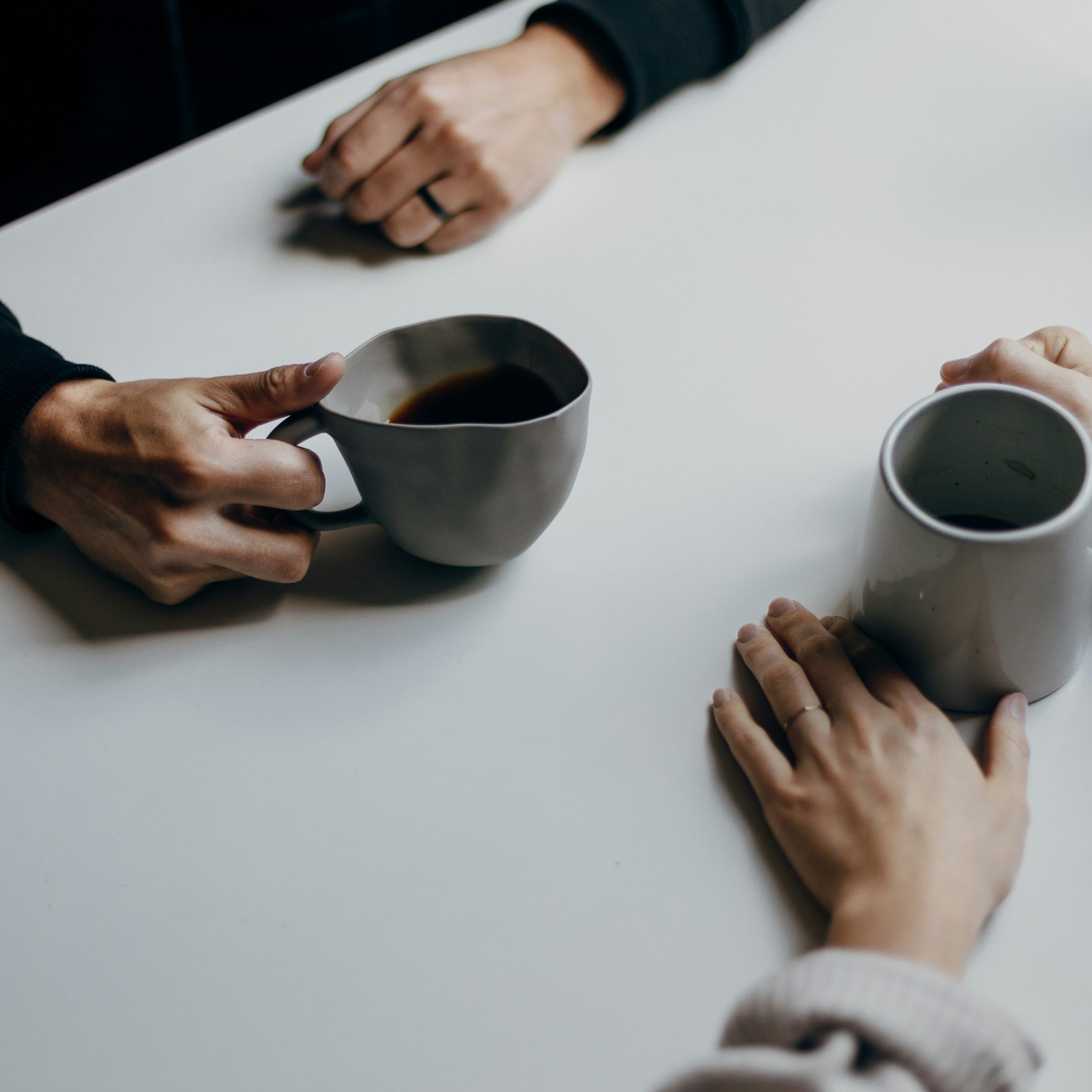 Hands around coffee cups on a table, symbolizing connection and support